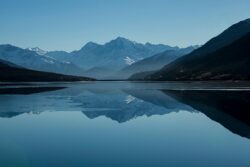 Snow-capped mountains reflected in a calm alpine lake Mountain lake reflecting snow-capped peaks under blue sky